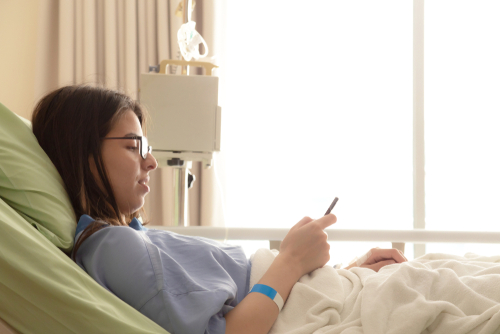 beautiful young patient women lying in hospital bed and smiling with smart mobile phone while recovering in hospital-img-blog